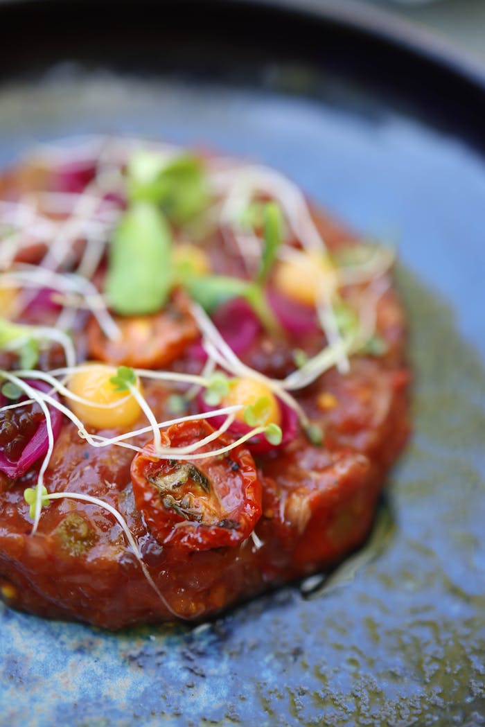 Delicious beef tartare garnished with cherry tomatoes and sprouts on a stylish plate.