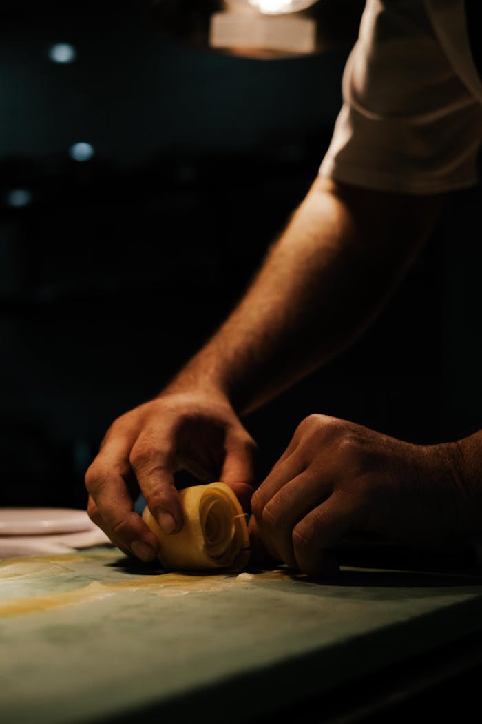 Close-up of hands making fresh pasta in dimly lit kitchen.